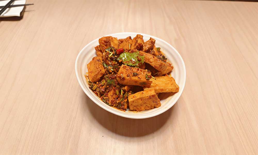 Spicy fried tofu cubes with cilantro, chili, and herbs in white bowl