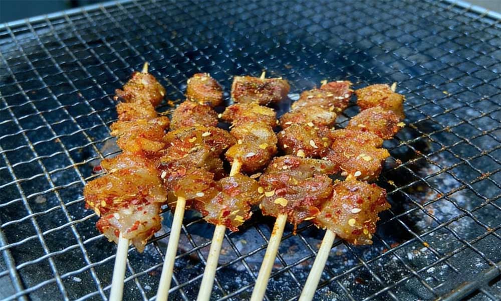 Grilled meat skewers with chili flakes and sesame seeds sizzling on charcoal grill