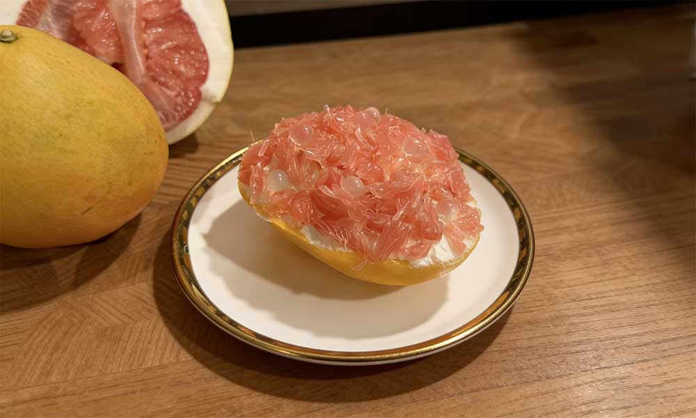 Peeled pink pomelo segments on gold-rimmed plate with whole pomelo beside
