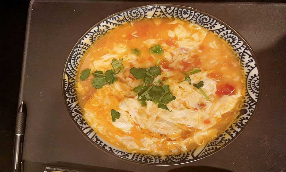 Tomato and egg drop soup garnished with fresh cilantro in patterned bowl