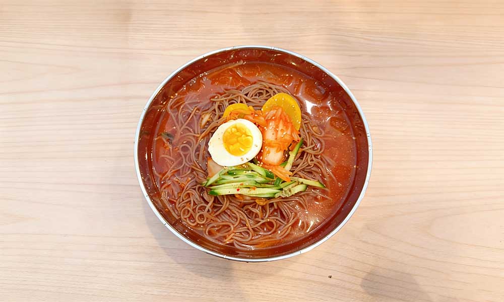 Korean cold buckwheat noodles in spicy broth with egg, kimchi, and cucumber